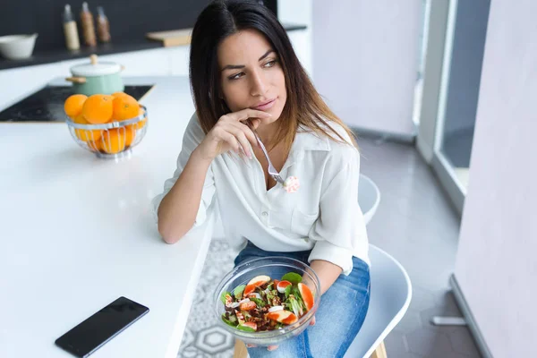 自宅の台所の椅子に座りながらサラダを食べてかなり若い女性のショット — ストック写真