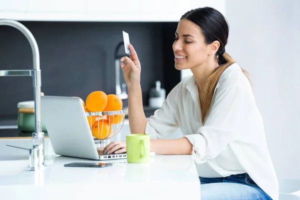 Mulher bonita compras on-line com cartão de crédito enquanto estiver na cozinha em casa . — Fotografia de Stock