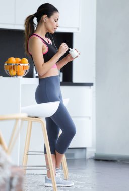 Atış sportif genç kadın mutfakta evde yoğurt yerken cep telefonu ile müzik dinlemek.