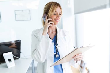 Bazı gazetelerde istişare gözden geçirirken cep telefonu kullanarak gülümseyen kadın doktor doz.