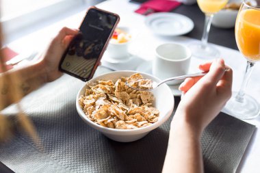 Genç kadının sahip otelin yemek salonunda kahvaltı ve manifatura onun smartphone ile yakın çekim.