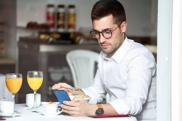 Yakışıklı Genç Adam Yeme Tahıl Ile Cep Telefonunu Otelin Yemek — Stok fotoğraf