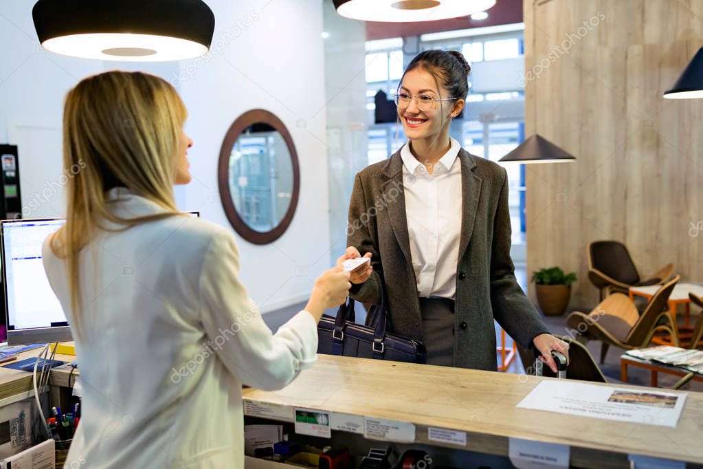 Shot of beautiful businesswoman takes room key card and doing check-in at the hotel reception.