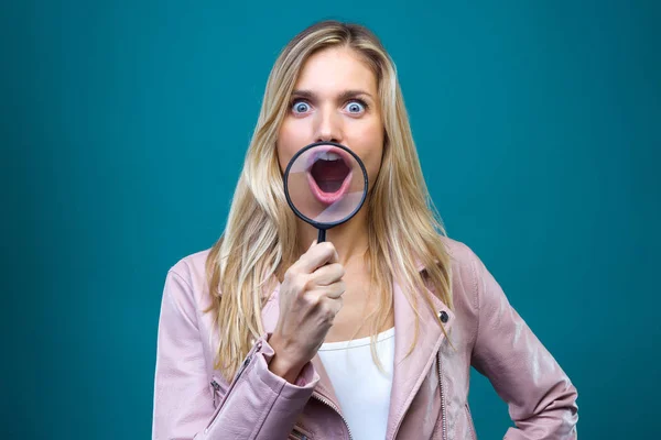 Divertida joven mujer mostrando su boca a través de lupa sobre fondo azul . — Foto de Stock