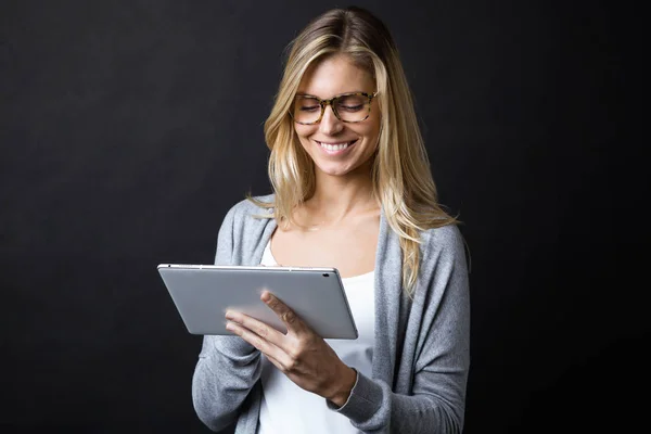 Lächelnd schöne junge Frau mit Brille, die mit digitalem Tablet auf schwarzem Hintergrund arbeitet. — Stockfoto