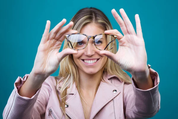 Mosolygó fiatal nő, tökéletes mosoly mutatja a kamera szemüveg át kék háttér. — Stock Fotó