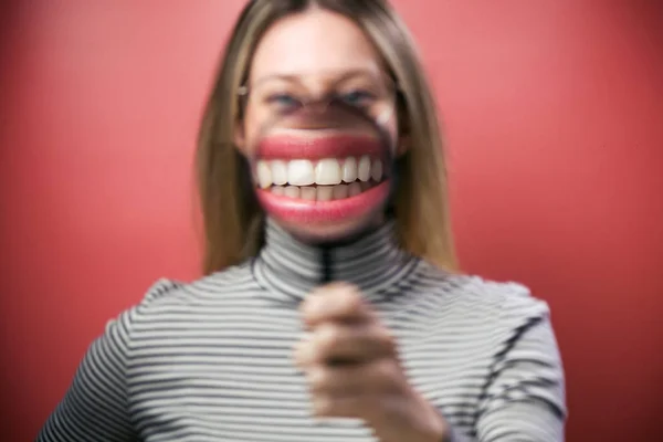 Divertida joven mujer mostrando su boca a través de lupa sobre fondo rosa . — Foto de Stock