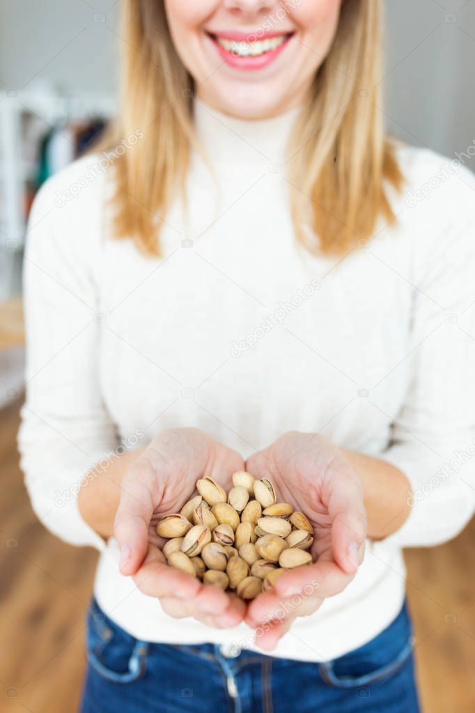 Happy young woman hands holding pistachios nuts at home.