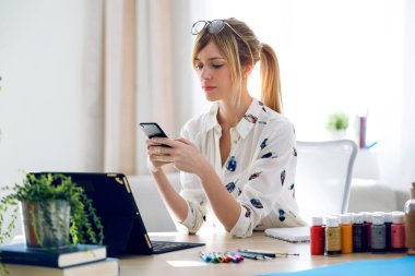Ofiste onu cep telefonu ile manifatura neşeli güzel genç tasarımcı kadın.