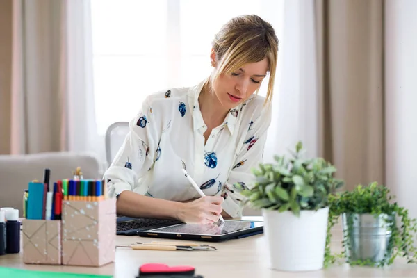 Концентрированная красивая молодая дизайнерша рисует что-то на своей цифровой планшете в офисе . — стоковое фото