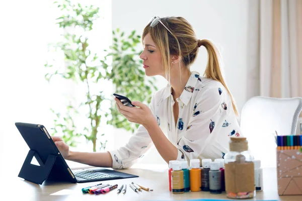 愉快美丽的年轻设计师女子在办公室拿着手机的同时, 拿着数字平板电脑工作. — 图库照片
