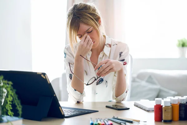 Уставшая молодая женщина с головной болью работает со своим цифровым планшетом в офисе . — стоковое фото
