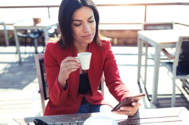 Kendine güvenen genç kadın bir kafe teras wodden tablo cep telefonu ile mesaj sırasında kahve içme.