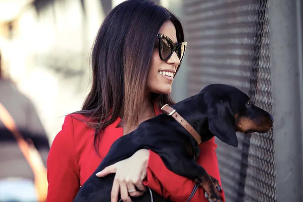 Attractive young woman holding her small dog while walking to the street. — Stock Photo, Image