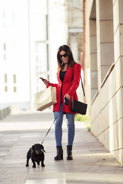Şehrin küçük köpeği ile alışveriş yaparken yürüyen serin güzel genç kadın. — Stok fotoğraf