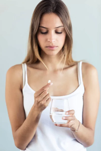 Depressive junge Frau nimmt Tabletten vor grauem Hintergrund. — Stockfoto