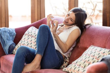 Evde kanepede otururken onu akıllı telefon ve parlatma çivi konuşurken güzel genç kadın.