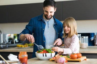 Onun küçük sevimli kızı ile çekici genç adam evde mutfakta birlikte salata yapma.