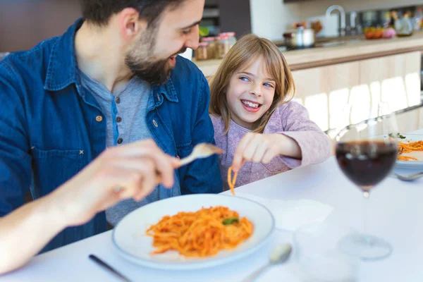 ハンサムな若い父親と彼女の美しい自宅の台所で昼食のためにトマトソースとパスタを食べながら楽しんで. — ストック写真