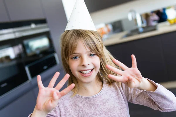 Fröhliches kleines Mädchen, das acht Finger hochhält, während es seinen Geburtstag zu Hause in der Küche feiert. — Stockfoto