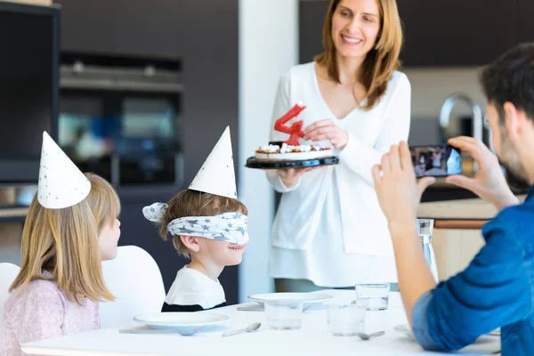 Χαριτωμένο οικογένεια γιορτάζει τα γενέθλια των παιδιών, ενώ οι γονείς καλύπτοντας τα μάτια του γιού στην κουζίνα στο σπίτι. — Φωτογραφία Αρχείου