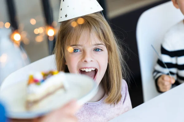 Engraçado menina surpresa e se divertindo com bolo de aniversário na cozinha em casa . — Fotografia de Stock