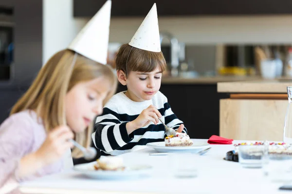 Pequenas crianças bonitos comer bolo de aniversário na cozinha em casa . — Fotografia de Stock