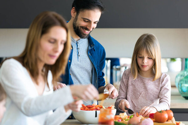 Attractive young man with her little cute daughter making salad together on kitchen at home.