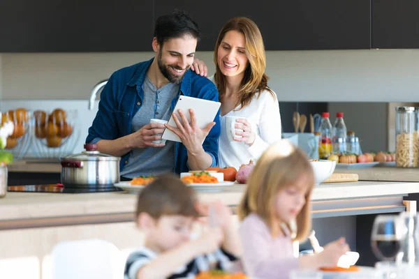 自宅の台所で息子と昼食をとりながらデジタルタブレットを使用して魅力的な若いカップル. — ストック写真