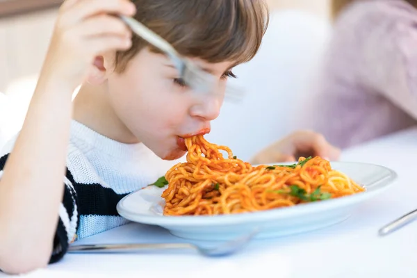 Głodny mały chłopiec jedzenia spaghetti z sosem pomidorowym w kuchni w domu. — Zdjęcie stockowe