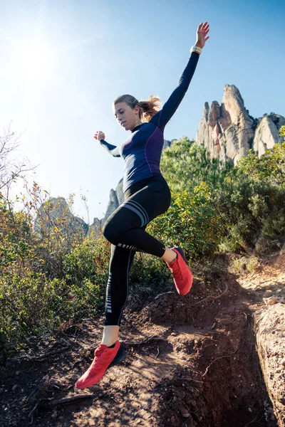 Fiatal fitness nő nyomvonal futó futás és ugrás sziklás hegyen. — Stock Fotó