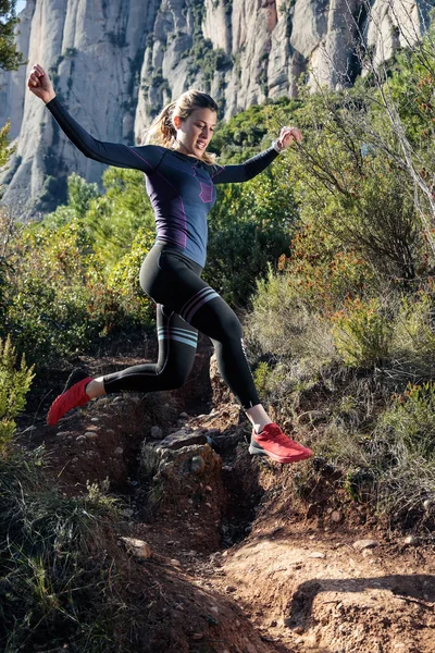 Young fitness woman trail runner running and jumping on rocky mountain. — Stockfoto