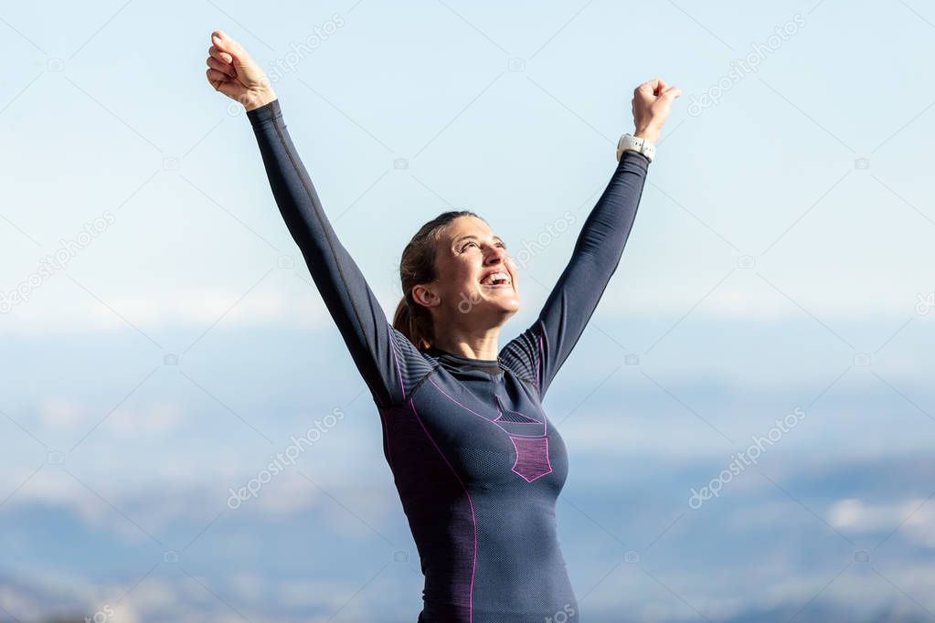 Trail runner with open arms raised while enjoying nature on mountain peak.