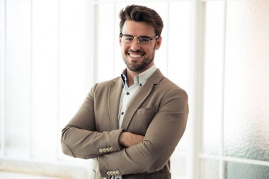 Yakışıklı genç iş adamı ofiste dururken kameraya bakıyor.