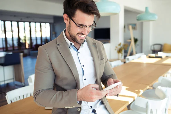 Bello giovane uomo d'affari che usa il suo smartphone mentre è seduto sul tavolo in ufficio . — Foto Stock