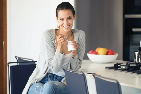 Pretty young woman looking at camera while eating yogurt in the kitchen at home. — Stock Photo, Image