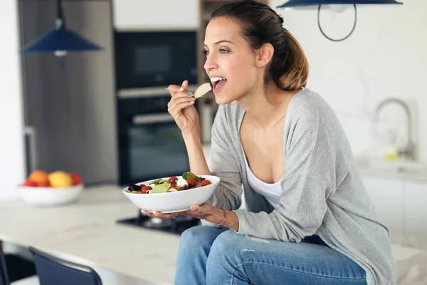 Mujer bastante joven comiendo ensalada mientras está sentado en la cocina en casa . —  Fotos de Stock