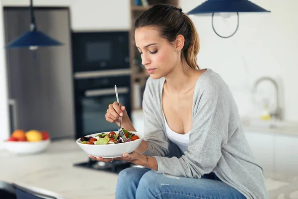 예쁜 젊은 여자 먹는 샐러드 동안 에 앉아 있는 부엌 에 홈. — 스톡 사진