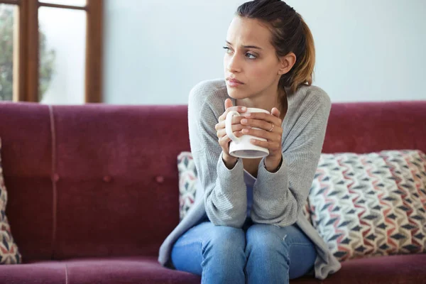 Mujer joven deprimida pensando en sus problemas mientras bebe café en el sofá en casa . —  Fotos de Stock