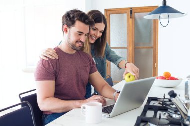 Güzel güzel genç çift kendi dizüstü bilgisayar kullanarak ve evde mutfakta kahvaltı yapıyor.
