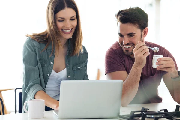 Beau beau jeune couple en utilisant leur ordinateur portable et prendre le petit déjeuner dans la cuisine à la maison . — Photo