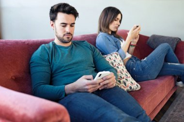 Kızgın genç çift evde kanepede otururken bir tartışma dan sonra telefon kullanarak birbirlerini görmezden.