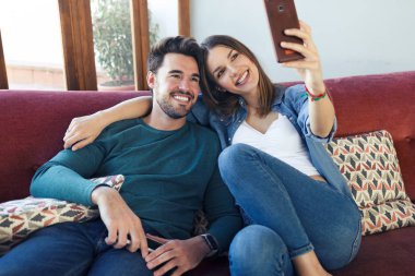 Mutlu genç çift evde kanepede otururken akıllı telefon ile selfie çekerken.