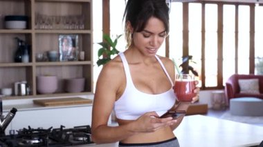 Evde mutfakta çilek smoothie içerken onun cep telefonu kullanarak sportif genç kadının Video.