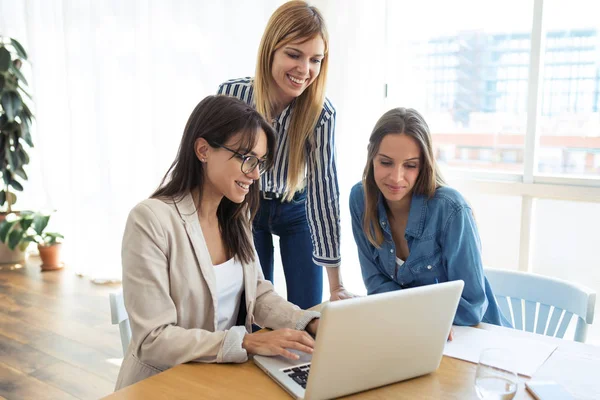 Mujer de negocios bastante joven mostrando el progreso del trabajo en el ordenador portátil a los compañeros de trabajo en la oficina . — Foto de Stock