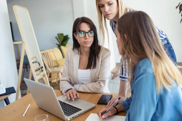 Całkiem młoda businesswoman pokazując postęp pracy na laptopie do współpracowników w biurze. — Zdjęcie stockowe