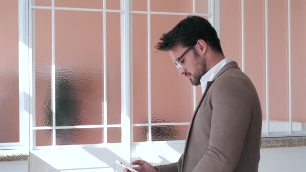 Bonito jovem homem de negócios usando seu smartphone enquanto se senta na mesa no escritório . — Vídeo de Stock