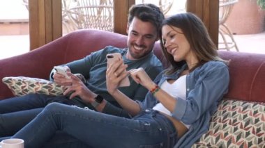 Evde kanepede otururken cep telefonu kullanarak güzel genç çift Video.