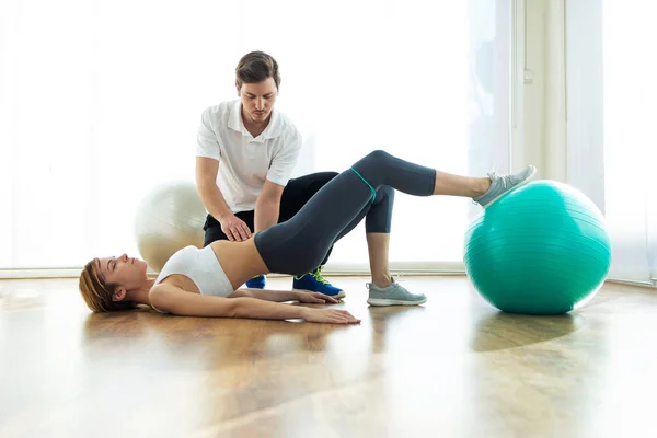 Fisioterapeuta ayudando al paciente a hacer ejercicio sobre la pelota de fitness en la sala de fisioterapia . — Foto de Stock