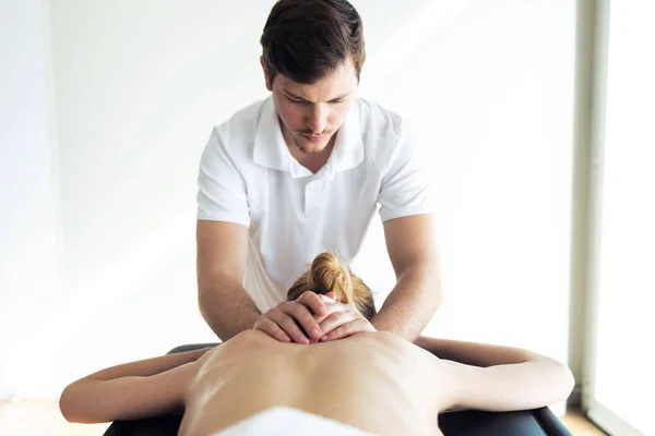 Joven fisioterapeuta haciendo un tratamiento de espalda al paciente en una sala de fisioterapia . — Foto de Stock